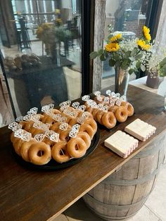 there are many doughnuts on the table with flowers in the vase behind them