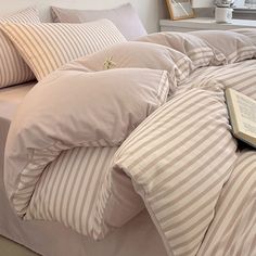 a book is laying on top of a bed with striped comforter and pillows in front of a window