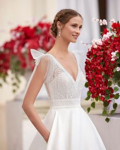 a woman in a white wedding dress standing next to red and pink flowers with her hands on her hips