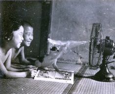 an old photo of two people sitting at a table with a fan and magazine in front of them