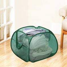 a green storage bag filled with clothes on top of a hard wood floor next to a chair