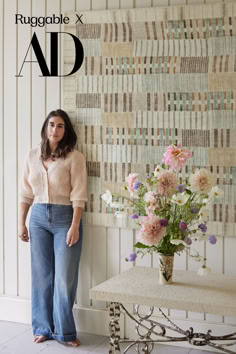 a woman leaning against a wall next to a vase with flowers in it and the words ruggable ad above her