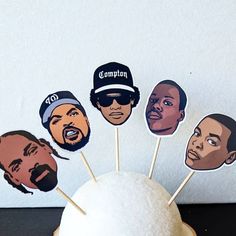 a cupcake topper with the faces of five different men on it, including one man wearing a hat