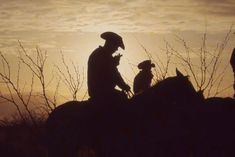 two men riding horses with a dog in the background at sunset or dawn, silhouetted against an overcast sky