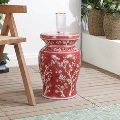 a red vase sitting on top of a wooden floor next to a chair and potted plant