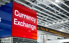 a red and blue sign that says currency exchange at an airport terminal with other signs in the background