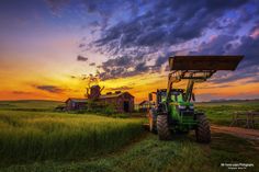 a tractor parked in front of a barn at sunset