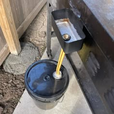 a bucket with a yellow straw sticking out of it next to a metal container on the ground