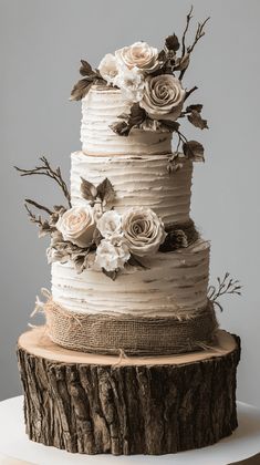 a three tiered cake with white flowers and branches on top is sitting on a tree stump