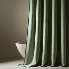 a green curtain hanging from a window next to a white bowl with a plant in it