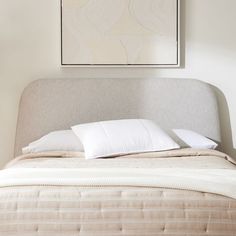 a bed with two pillows on top of it and a painting above the headboard