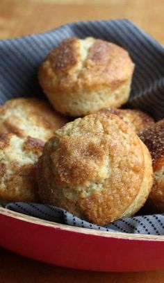 four muffins in a red bowl on a wooden table with a blue cloth