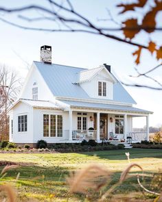 a large white house with a porch and covered in metal roofing on the front lawn