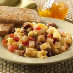 an egg salad with sausage and tomatoes in a white bowl next to toasted bread