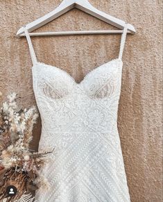 a wedding dress hanging on a hanger next to dried flowers