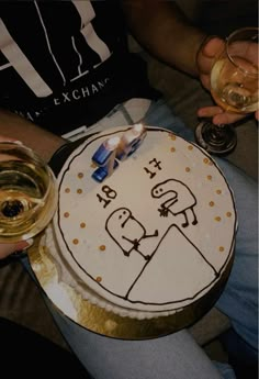 a person holding a cake with candles on it and wine glasses in front of them