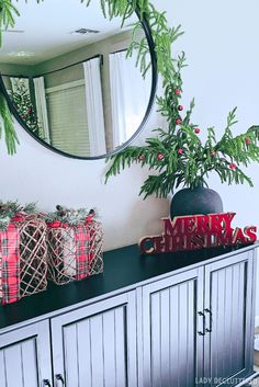 christmas decorations on top of a dresser in front of a round mirror and evergreen branches