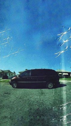 a black van parked in the middle of a parking lot with blue sky and clouds