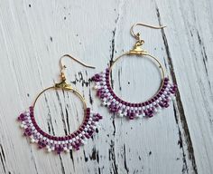 a pair of purple and white beaded hoop earrings sitting on top of a wooden table