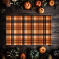 a plaid table cloth surrounded by pumpkins and gourds on a wooden surface