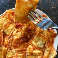 a fork is stuck into some ravioli on a white plate with sauce and cheese