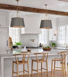 a kitchen with two pendant lights hanging from the ceiling and three bar stools at the island