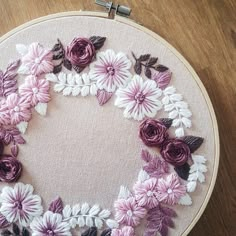 a close up of a embroidery on a wooden surface with flowers in the center and leaves around it