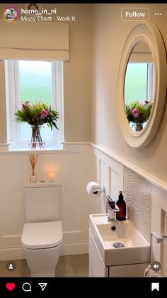 a white toilet sitting next to a bathroom sink under a window with flowers in it