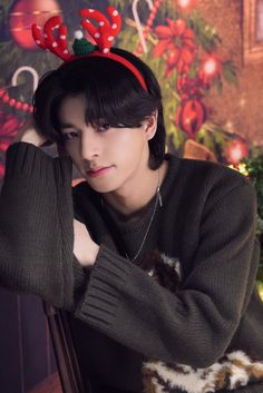 a woman wearing a reindeer antlers headband sitting in front of a christmas tree