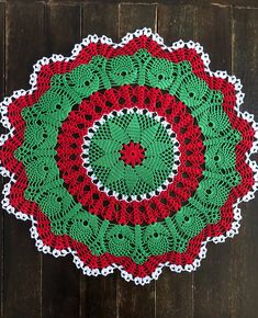 a crocheted doily with a red and green design on it sitting on a wooden surface