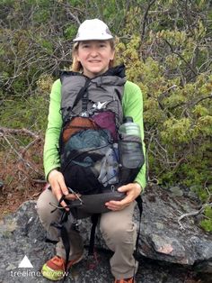 a woman sitting on top of a rock with a backpack and water bottle in her hand