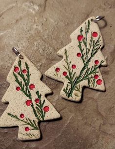 two ceramic christmas trees with red berries and green leaves on them, sitting on a stone surface