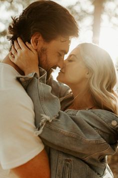 a man and woman kissing each other in the woods with sun shining through trees behind them