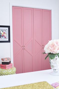 a vase with pink flowers sitting on top of a white table next to two doors