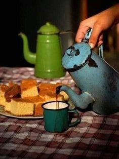 a person pouring tea into a blue teapot on top of a table next to bread