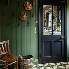 a green room with a black door and two hats hanging on the wall next to a wooden chair