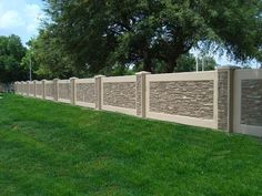 a stone fence with grass and trees in the background