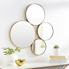 three circular mirrors mounted on the wall above a white table with a gold vase and potted plant