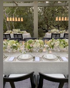 a long table with white and green flowers on it is set for an outdoor dinner