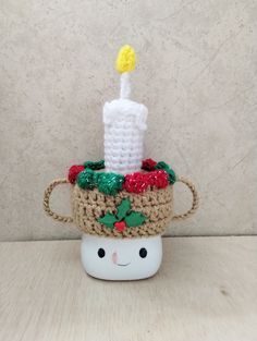 a crocheted cup with a lit candle in it on top of a table