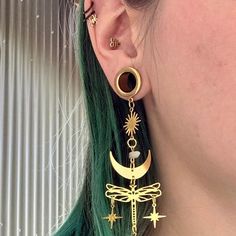 a close up of a person wearing ear rings with dragonfly and moon charms on them