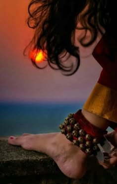 a woman's feet with bracelets on the beach at sunset