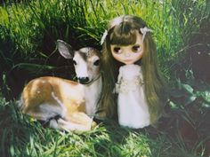 a doll is sitting next to a deer in the grass