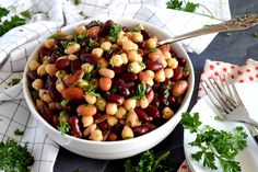 a white bowl filled with beans and parsley on top of a table next to silverware