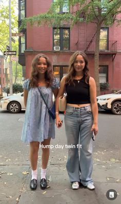 two young women standing on the sidewalk in front of a red brick building, holding hands