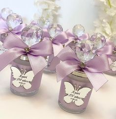 three small jars with purple bows and crystal balls in them, each containing a butterfly