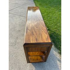 a wooden table sitting on top of a sidewalk next to a grass covered park area