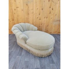 a white chaise lounge chair with fringe trim on the legs and back, against a wood paneled wall