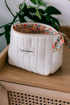 a white purse sitting on top of a wooden table next to a potted plant