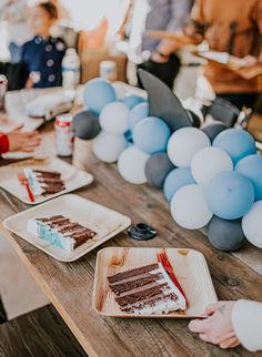 people sitting at a table with plates of cake and balloons on the table in front of them